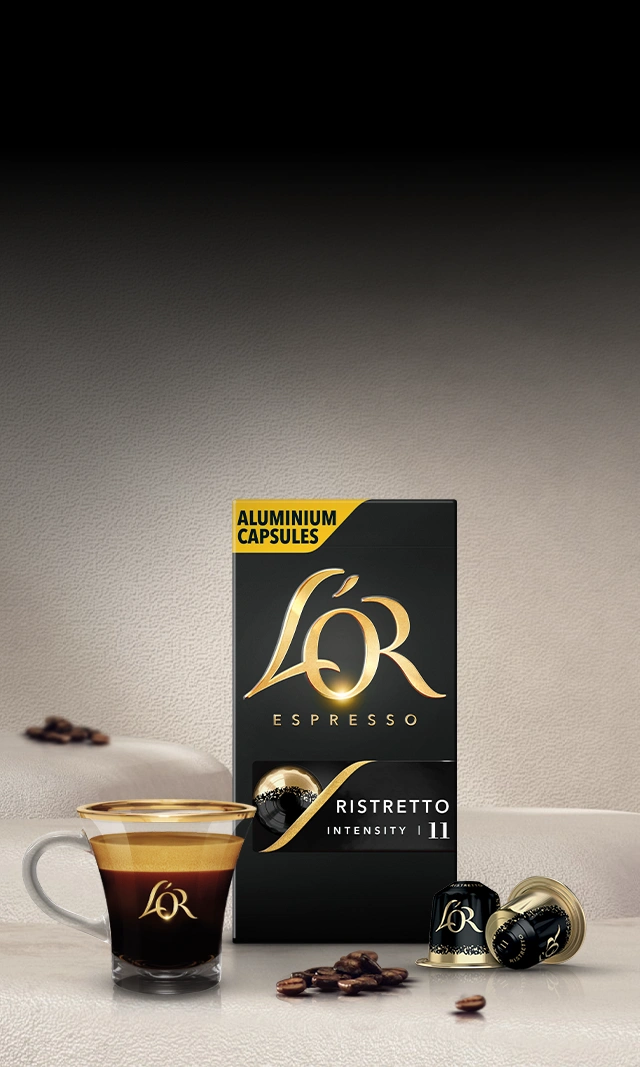 A L'OR Espresso-branded crema-rich coffee cup next to a pack of coffee capsules on a tabletop