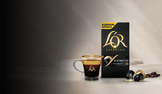 A L'OR Espresso-branded crema-rich coffee cup next to a pack of coffee capsules on a tabletop