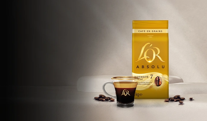 A L'OR Espresso-branded crema-rich coffee cup next to a pack of coffee beans on a tabletop
