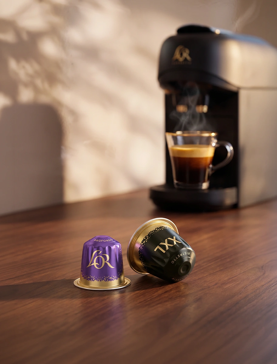 Black L'OR coffee machine brewing espresso beside purple and green coffee capsules.