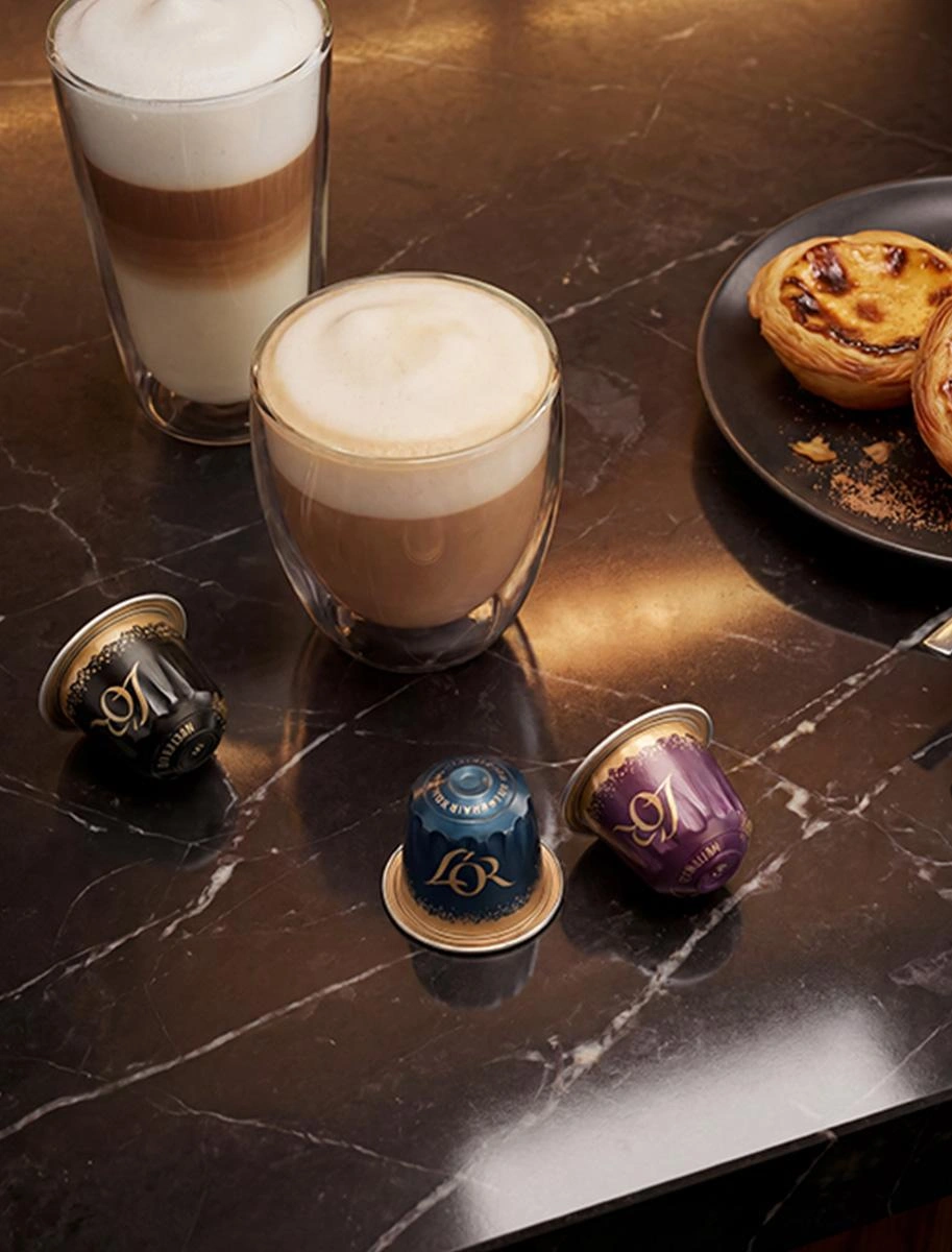 Two latte coffees in clear glasses with L’OR capsules and pastries.