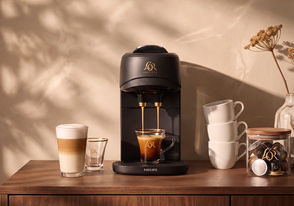 Black L'OR coffee machine with espresso glasses, a latte and milk jug on a kitchen counter.